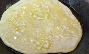 Naan in der Pfanne mit Knoblauchbutter betreichen