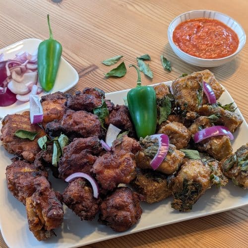 Fertiges Chicken 65 mit Hähnchen und Tofu, angerichtet mit roten Zwiebeln, grüner Chili und Dip